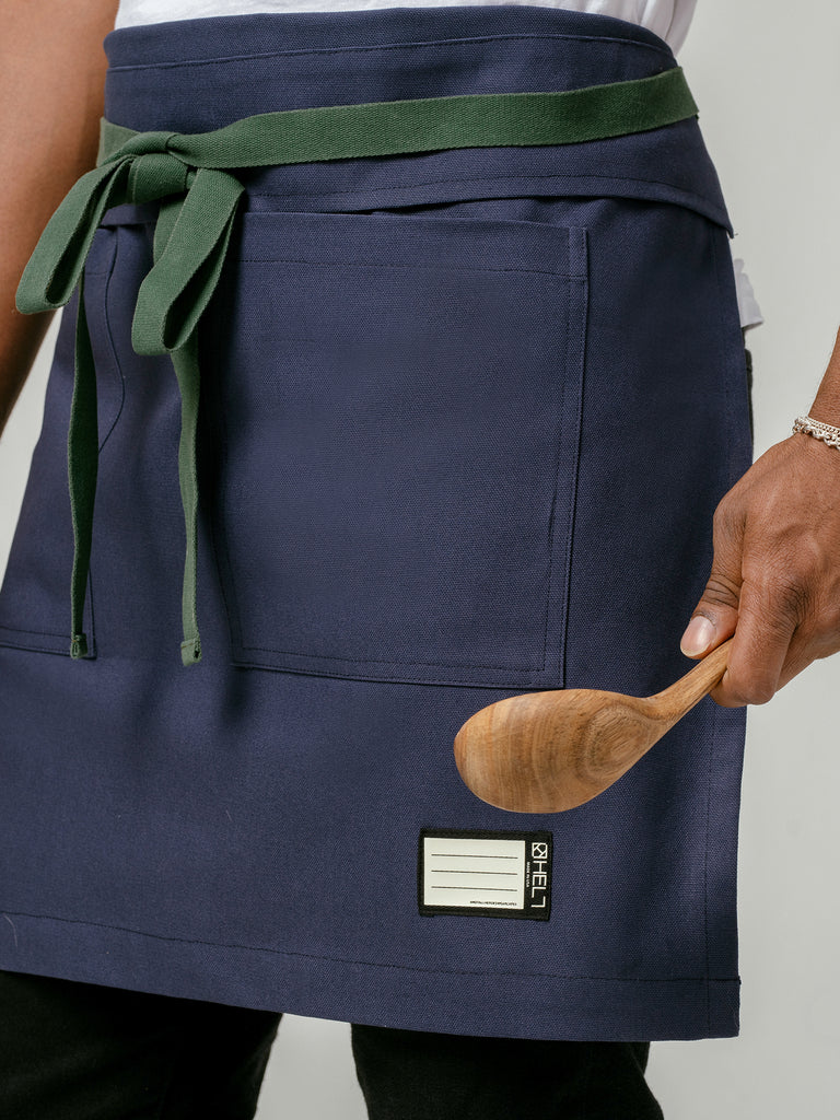Close up of man holding wooden spoon wearing Helt Studio's Deep Sea Navy Blue Bistro Apron.