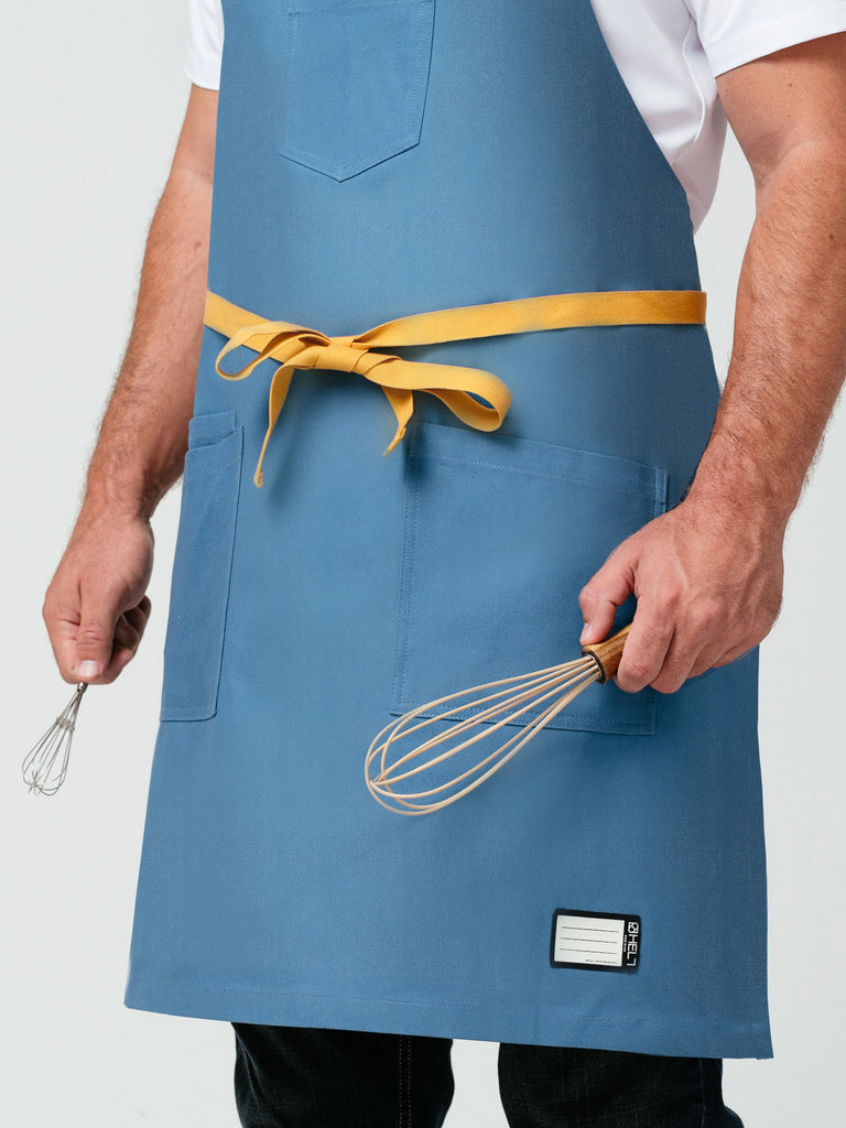 Close up of man modeling the Pot of Gold Bib Apron holding a whisk in each hand.