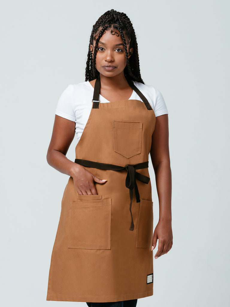 Woman placing a hand in her pocket modeling Helt Studio's Ranch Tan DWR Bib Apron.