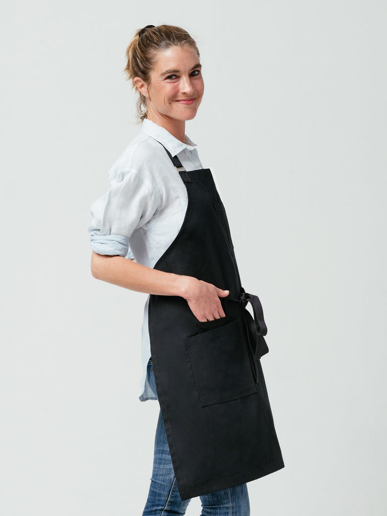 Side-view of woman with hand in her pocket modeling Helt's Raven Canvas Apron.