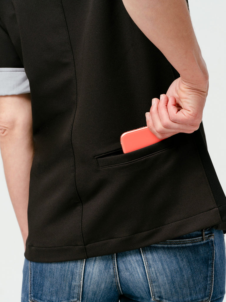 Close-up of woman placing phone in rear pocket of the Stephany Chef Coat in black.