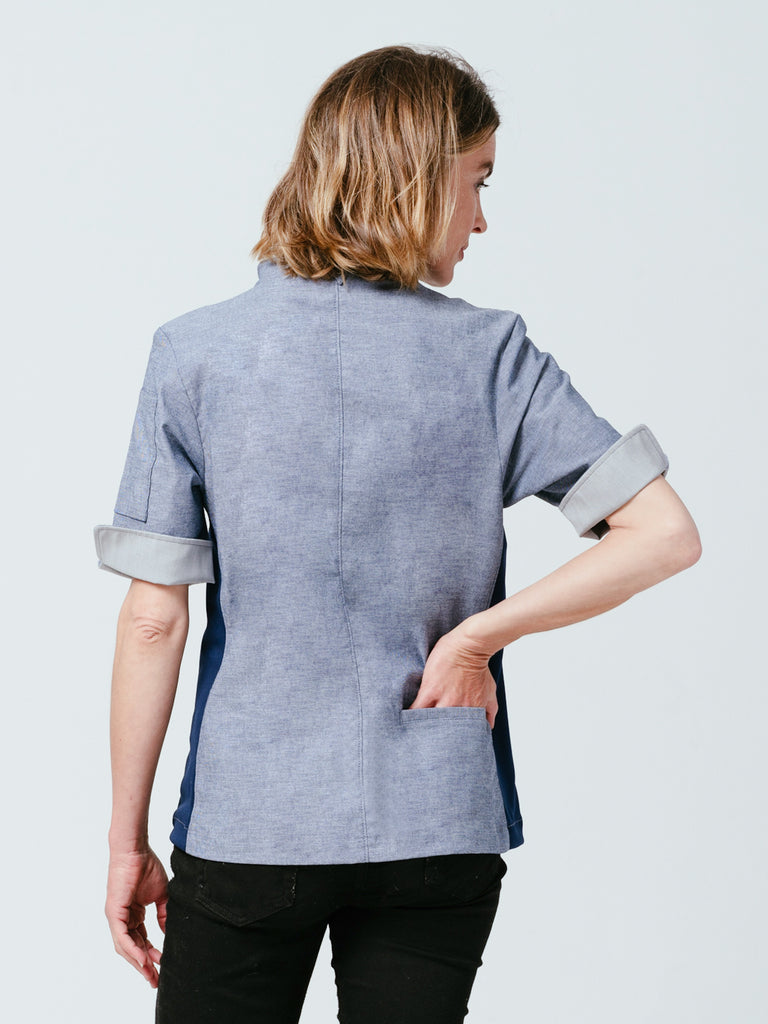 Woman with hand in rear pocket modeling the back of the Stephany Chambray Chef Coat.