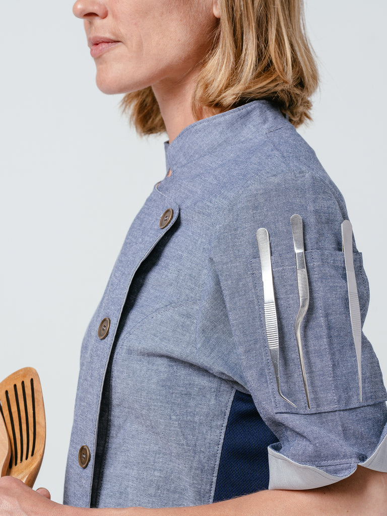Close-up of woman with utensils in sleeve pocket of the Stephany Chambray Chef Coat.