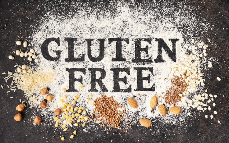Person wearing apron adding gluten-free flour to baking tin surrounded by ingredients