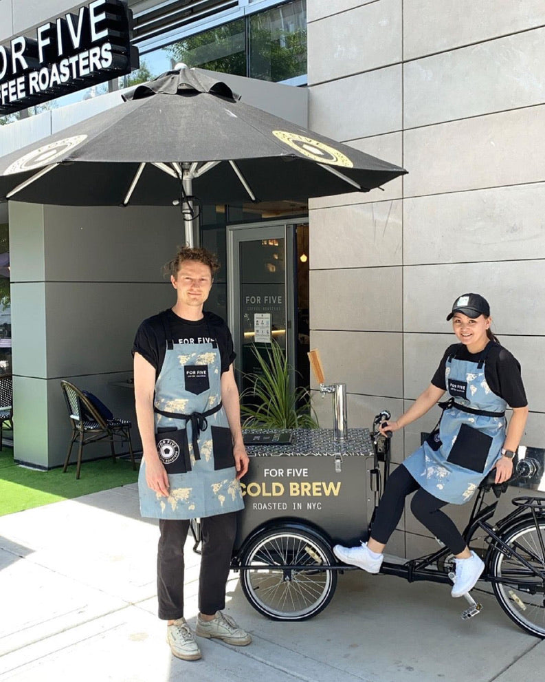 Two workers of For Fiver Coffee Roasters in uniforms posing next to mobile coffee-bike.