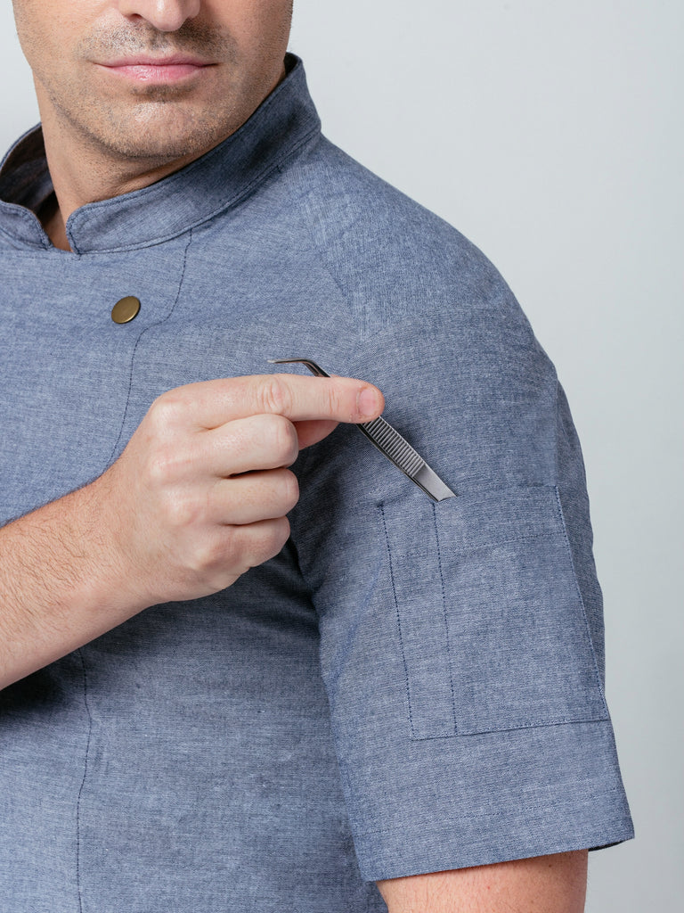 Close up of man placing tweezers in quick pocket on sleeve of Helt's Midtown Chef Coat Denim.