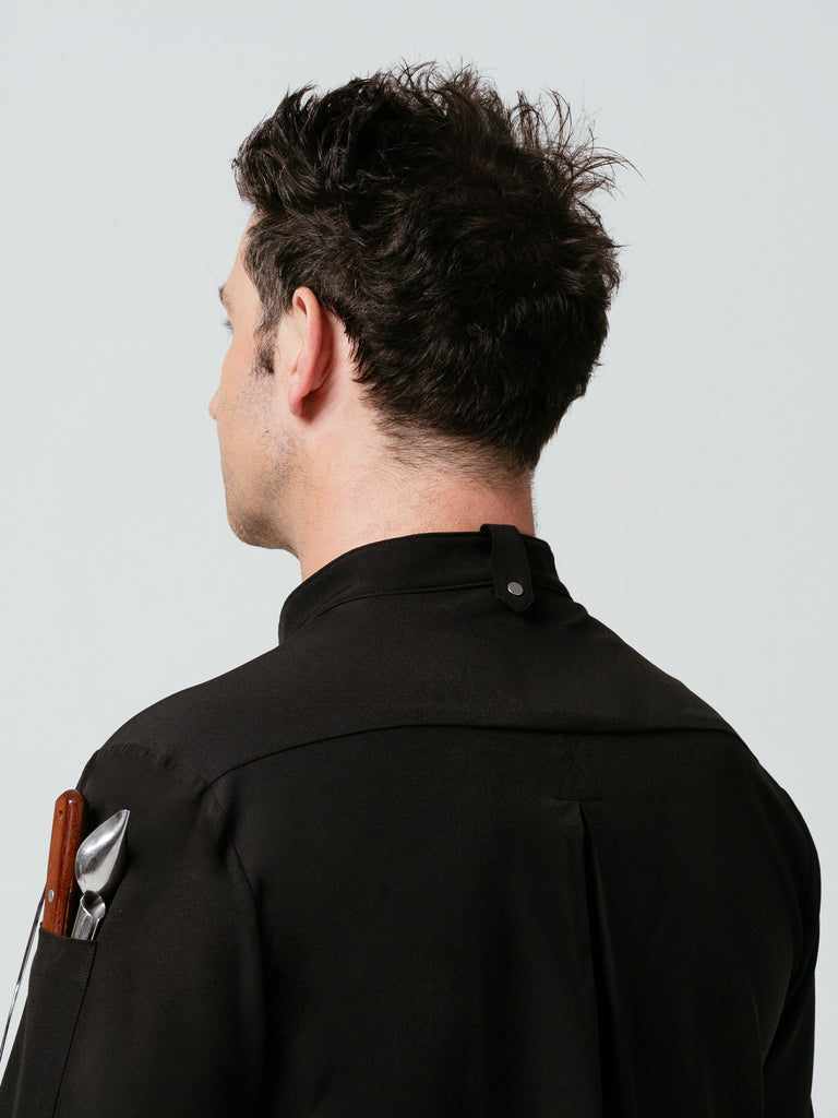 Close up of man modeling the rear collar of black Midtown Chef Coat with utensils in sleeve pocket.