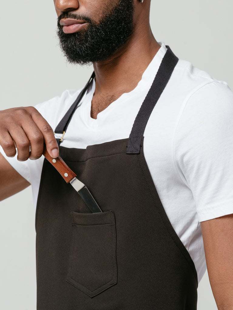 Close up of man placing knife in the chest pocket of Helt Studio's Noir CrewTech Apron.