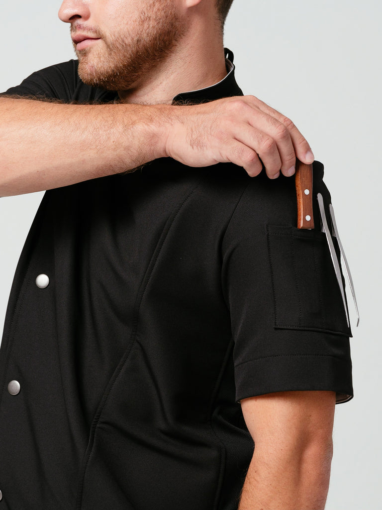 Close up of man placing utensils in quick-pocket on sleeve of the Hipster Chef Coat Noir.