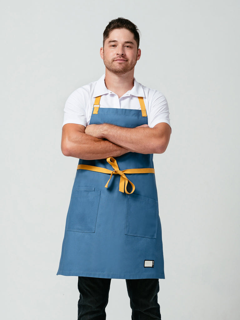 Man posing with arms crossed modeling Helt Studio's Pot of Gold Bib Apron.