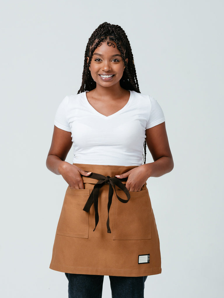 Woman with her hands in her pockets modeling Helt Studio's Ranch Tan DWR Bistro Apron.