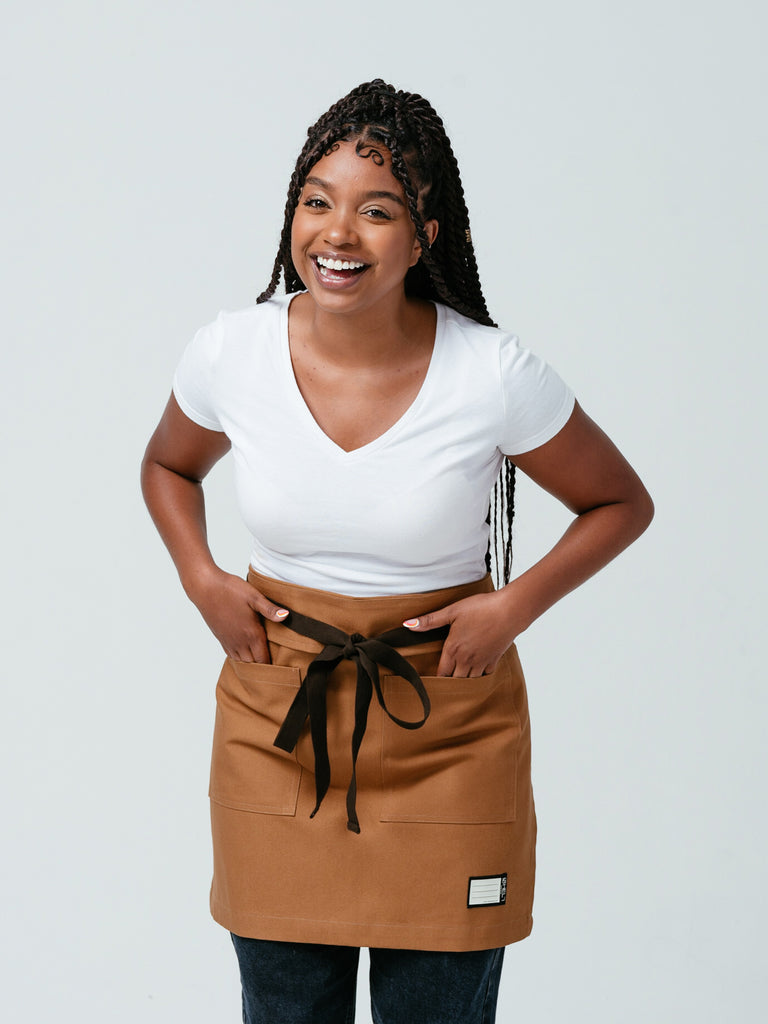 Woman with her hands in her pockets and laughing modeling the Ranch Tan DWR Bistro Apron.