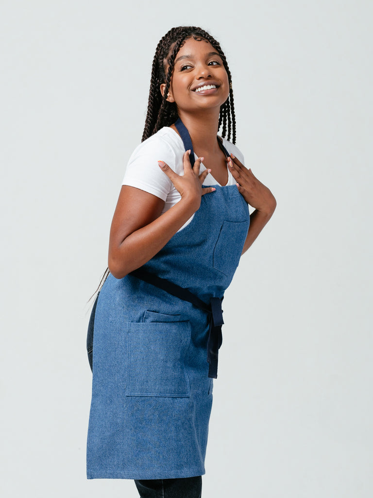 Woman with hands on her shoulders, smiling, modeling Helt Studio's Ocean Breeze Denim Apron.