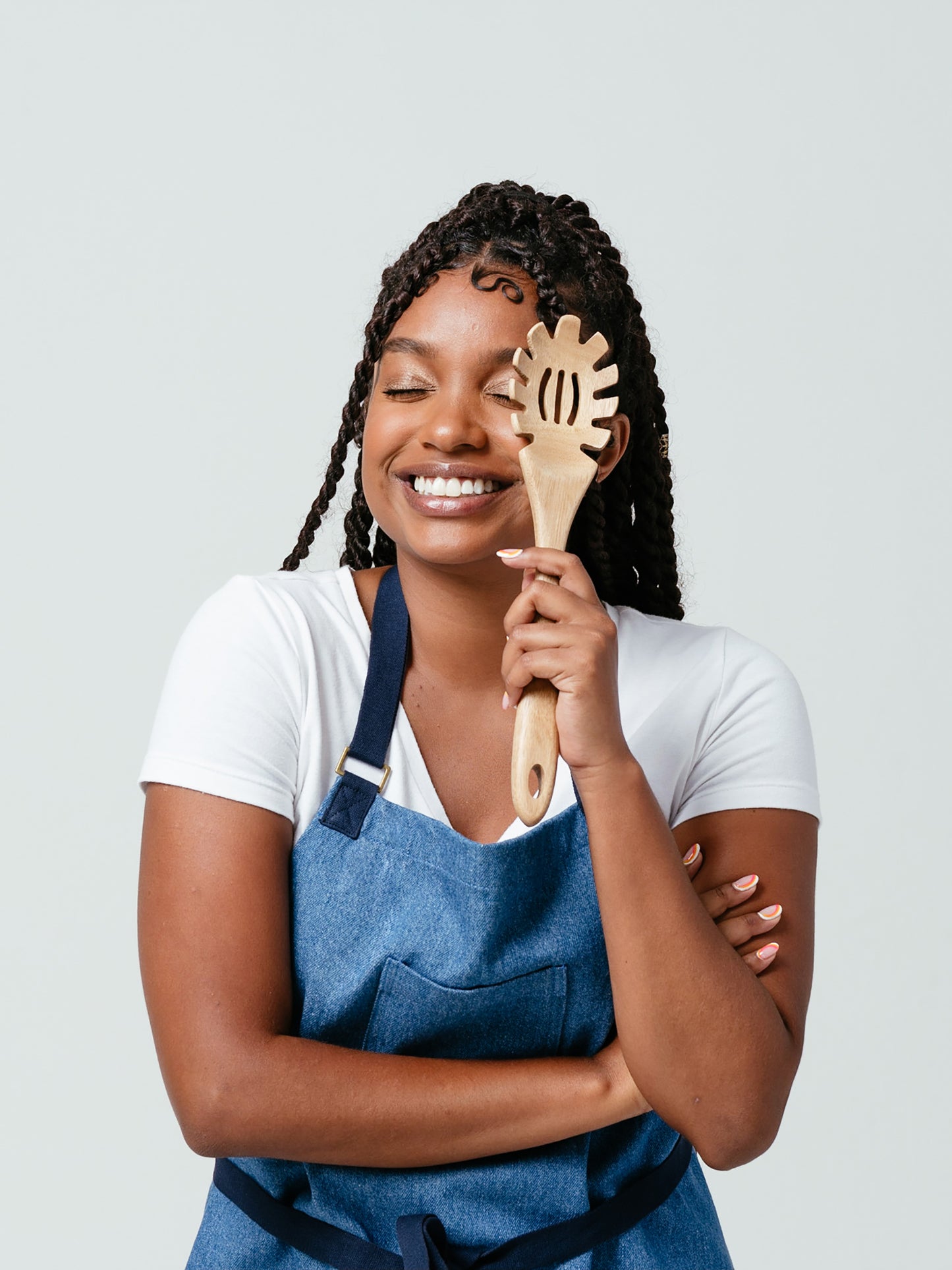 Woman holding wooden pasta fork over eye, laughing, modeling Helt's Ocean Breeze Denim Apron.