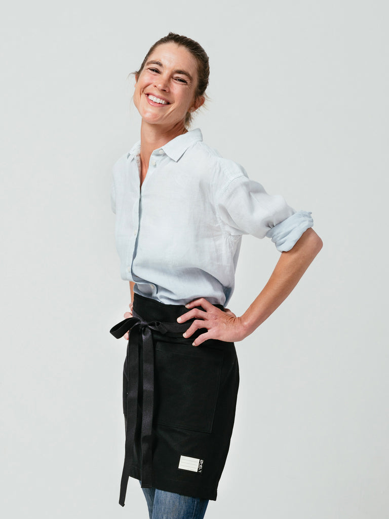 Woman with arms on her hips, laughing, modeling Helt Studio's Raven DWR Bistro Apron.