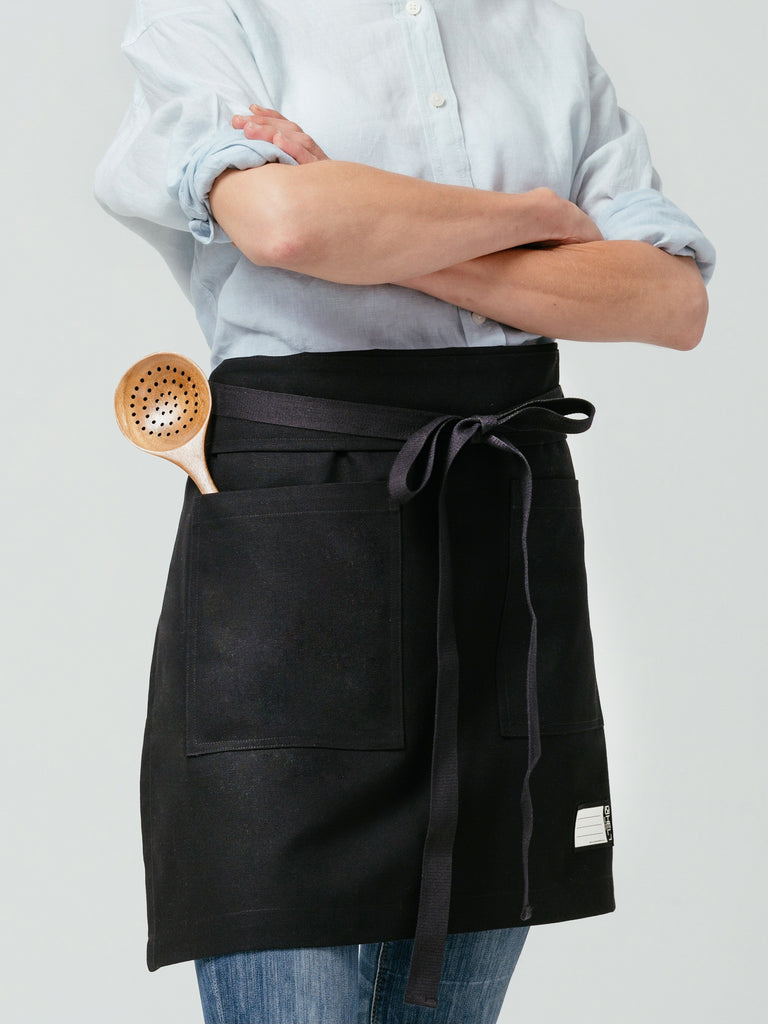 Close up of woman with a wooden spoon in her pocket of Helt Studio's Raven DWR Bistro Apron.