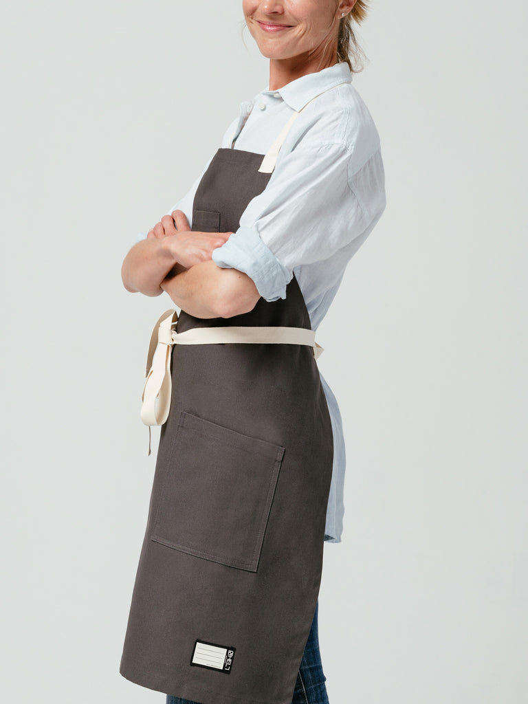 Side-view of woman with arms crossed modeling Helt Studio's Hardwood Briquette Bib Apron.