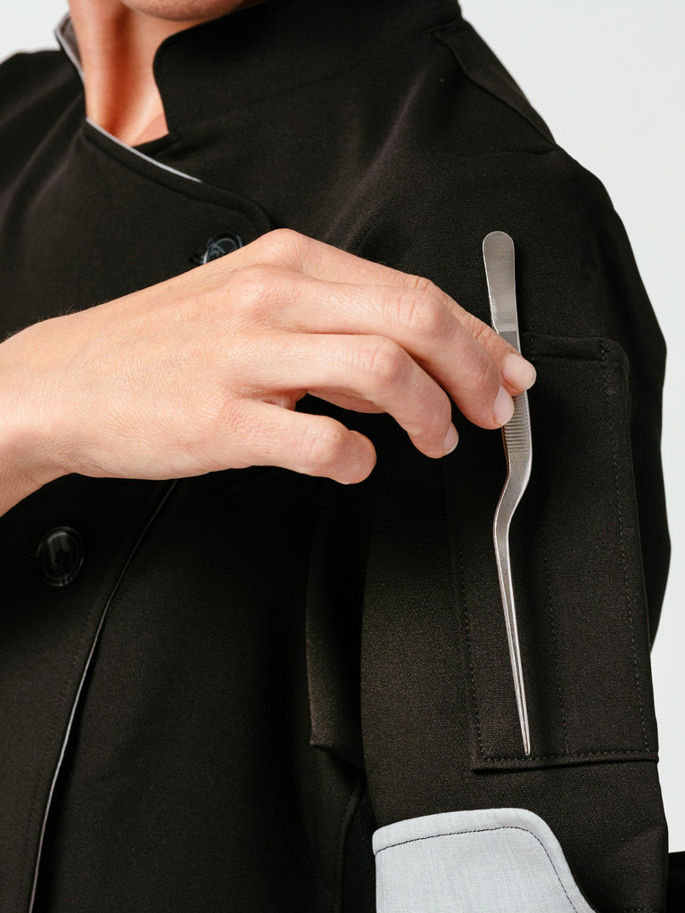 Close-up of woman placing utensils in pocket of sleeve on Helt's Stephany Chef Coat in black.