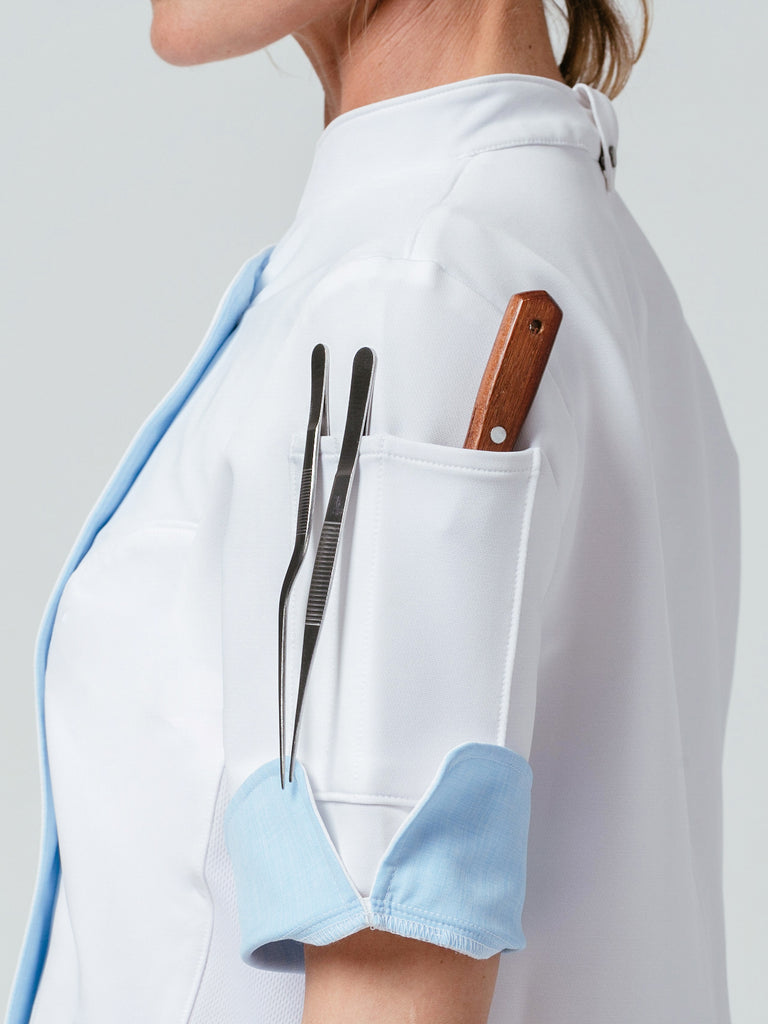 Close-up of woman with utensils in sleeve pocket of the Stephany Chef Coat in white.
